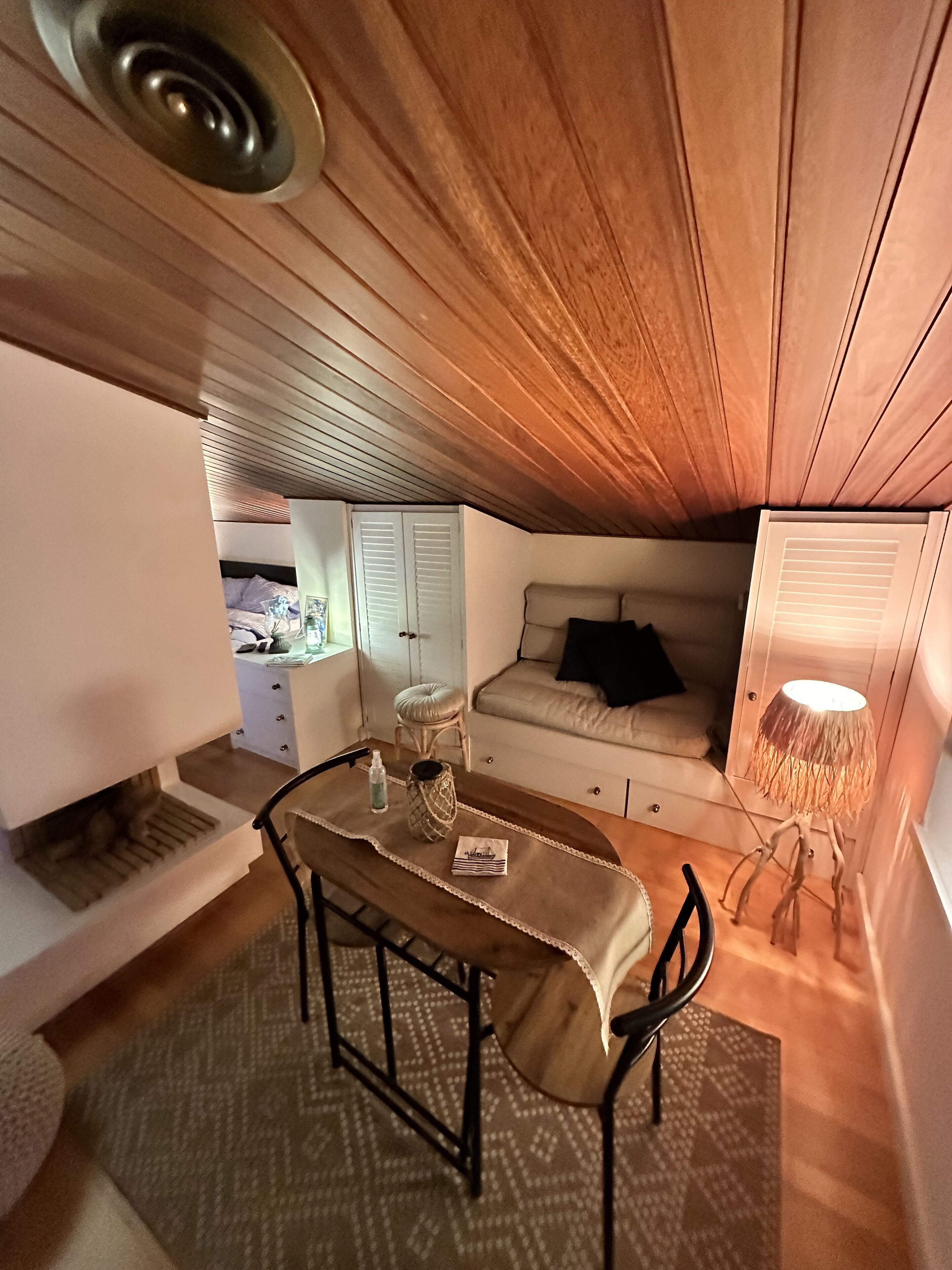 Ein kompakter, gemütlicher Raum mit Holzbalkendecke, einem kleinen Esstisch mit Stühlen, einer Couch und einer Lampe.