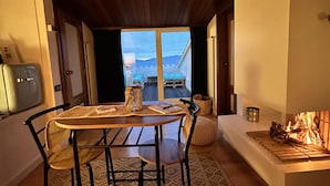 Ein gemütlicher Essbereich mit Tisch und Stühlen, einem Kamin und Blick ins Freie.