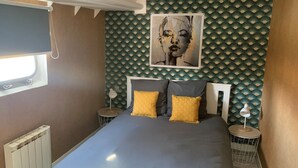 Un dormitorio con una cama, dos mesitas de noche, una ventana, un radiador y una pared con un dibujo de abanicos.
