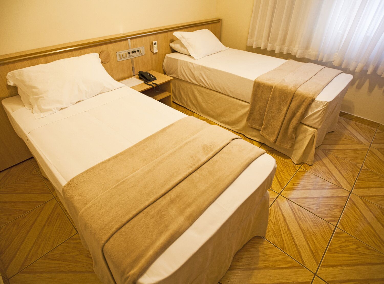 A hotel room with two beds, a bedside telephone, and a power outlet on the wall.
