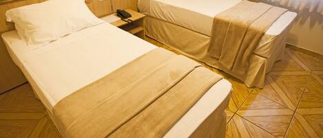 A hotel room with two beds, a bedside telephone, and a power outlet on the wall.