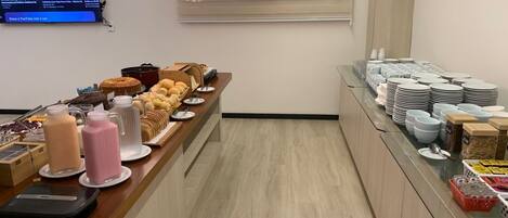 A buffet area with a variety of food items, a coffee station, and a counter with stacked plates and bowls.