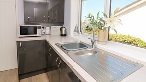 A modern kitchen with dark cabinets, a microwave, a bread maker, and a kettle. - Thornberry (Salcombe)