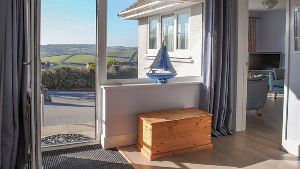 A room with a large sliding glass door leading to a scenic view of fields and a sailboat. - Thornberry (Salcombe)