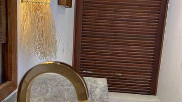 Un baño con lavamanos blanco, grifo dorado y aplique de pared con diseño de bambú.