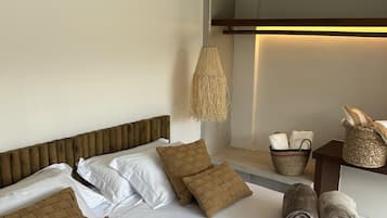 Habitación de hotel con cama, almohadas, lámpara colgante tejida y una pequeña mesa con una cesta y toallas.
