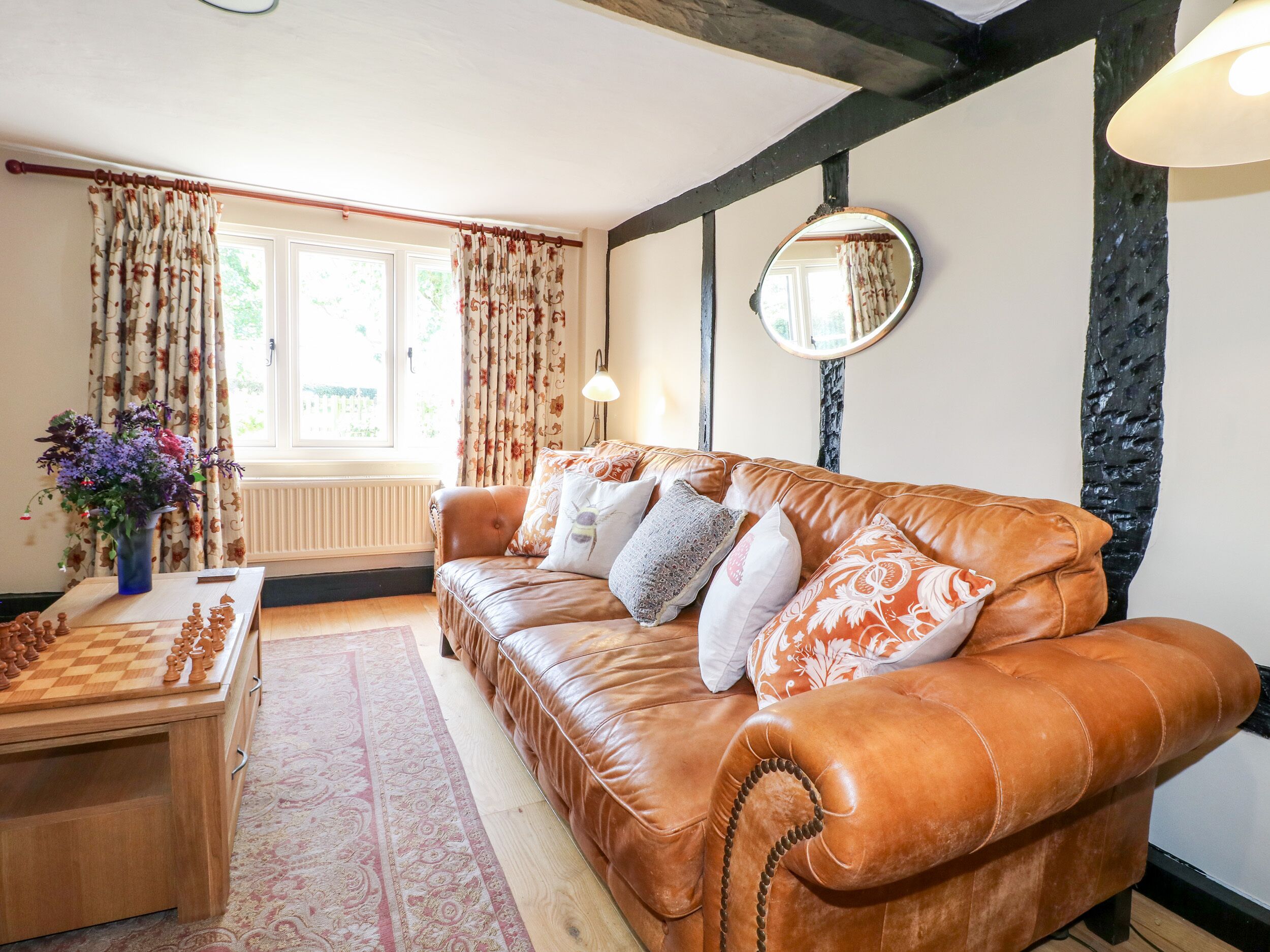 A cozy living room with a leather sofa, a chessboard, and a vase of flowers.