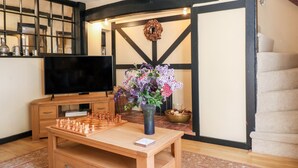 A cozy living room with a wooden coffee table, a chessboard, a flat-screen TV, and a vase with flowers. - Bluebell Cottage (Rugeley)