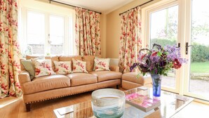 A living room with a leather sofa, a glass coffee table, and a vase of flowers. - Bluebell Cottage (Rugeley)
