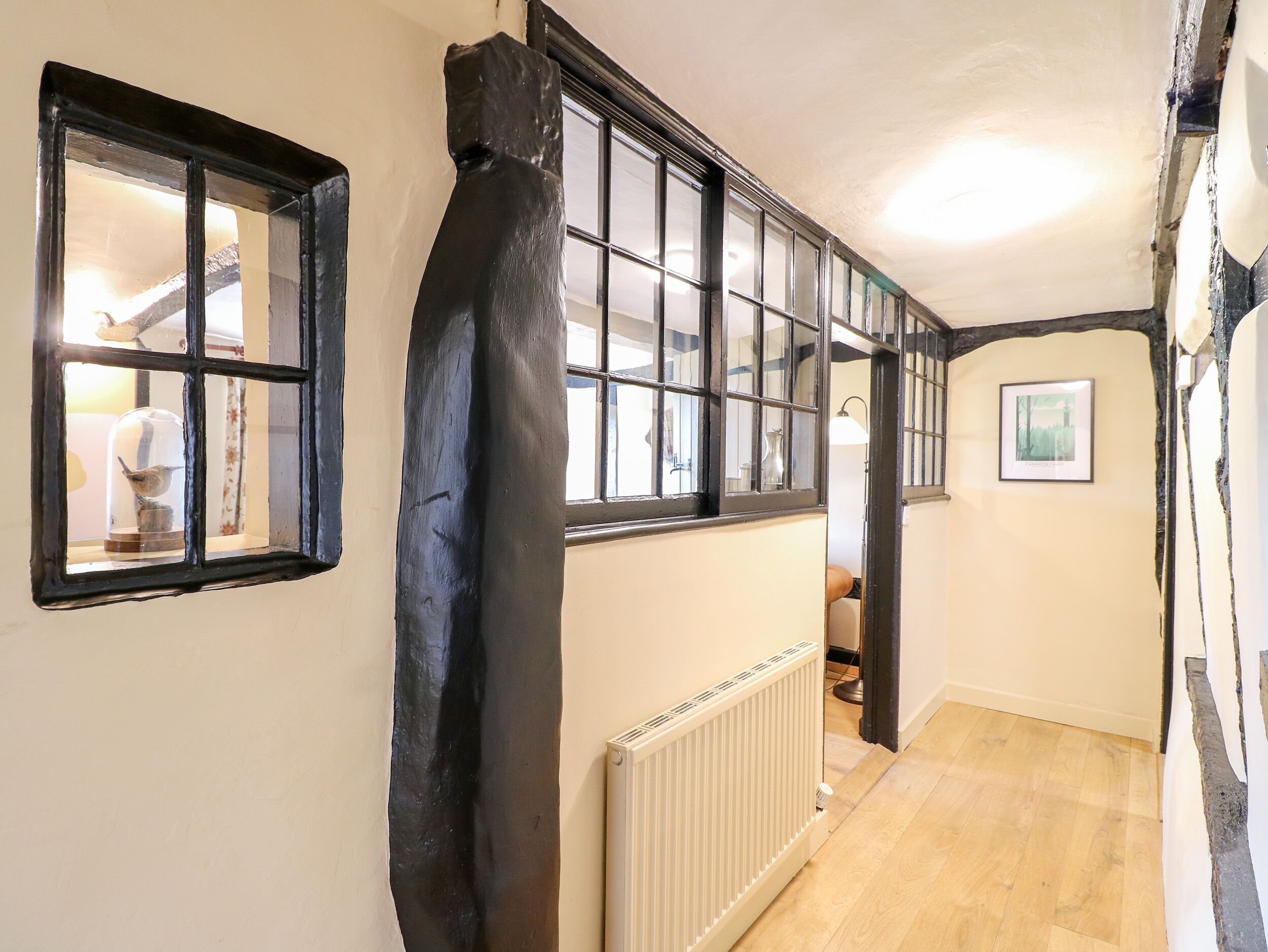 Un pasillo estrecho con ventanas de marco negro, un radiador y un cuadro en la pared.
