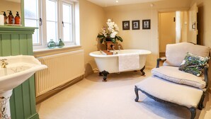 A bathroom with a bathtub, a sink, a chair, and a window. - Bluebell Cottage (Rugeley)