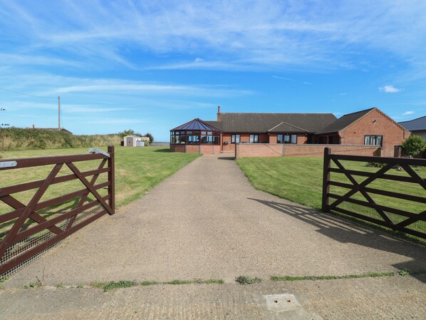 A gravel driveway leading to a brick building with a covered area and a small shed.