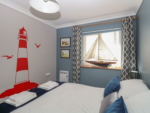 A bedroom with a bed, a window with curtains, a wall with a lighthouse mural, and a radiator.