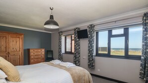 A bedroom with a bed, a wooden wardrobe, a television, and a window with a view of the sea.