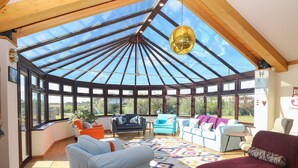 A spacious conservatory with a high ceiling, large windows, and a variety of seating options.