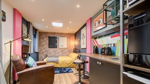 A compact living space with a brick wall, a sofa, a bed, a kitchenette, and a bar area.