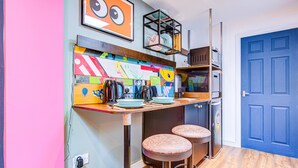 A kitchen with a colorful backsplash, two stools, a coffee machine, and a blue door.