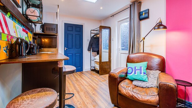 A cozy room with a brown leather sofa, a wooden floor, a blue door, and a kitchen area with a microwave and a coffee machine.