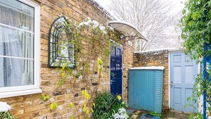 A brick house with a blue door, a blue shed, and a garden with plants and snow. - Cozy Brixton Hideaway – Cute & Convenient Stay - Pass the Keys (London)