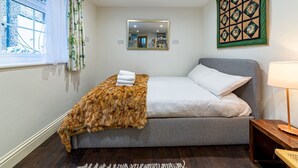 A bedroom with a bed, a window with curtains, a mirror, a wall art piece, and a bedside lamp. - Cozy Brixton Hideaway – Cute & Convenient Stay - Pass the Keys (London)