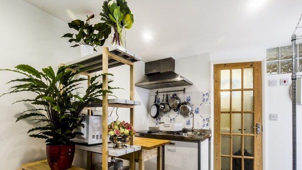 A compact kitchen with wooden shelves, a stove, and a window with a view. - Cozy Brixton Hideaway – Cute & Convenient Stay - Pass the Keys (London)