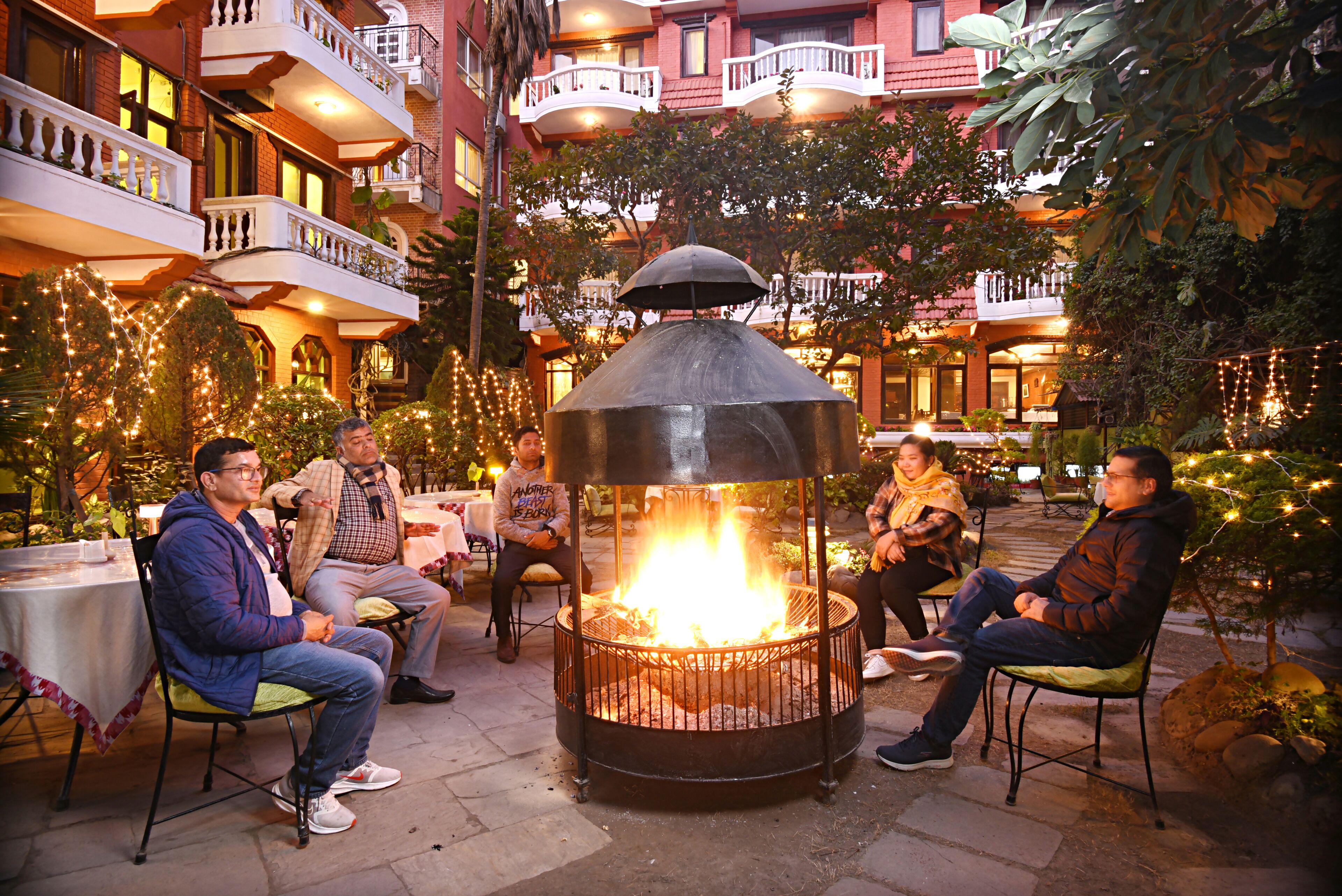 Un patio con una fogata, asientos al aire libre y un edificio con balcones al fondo.