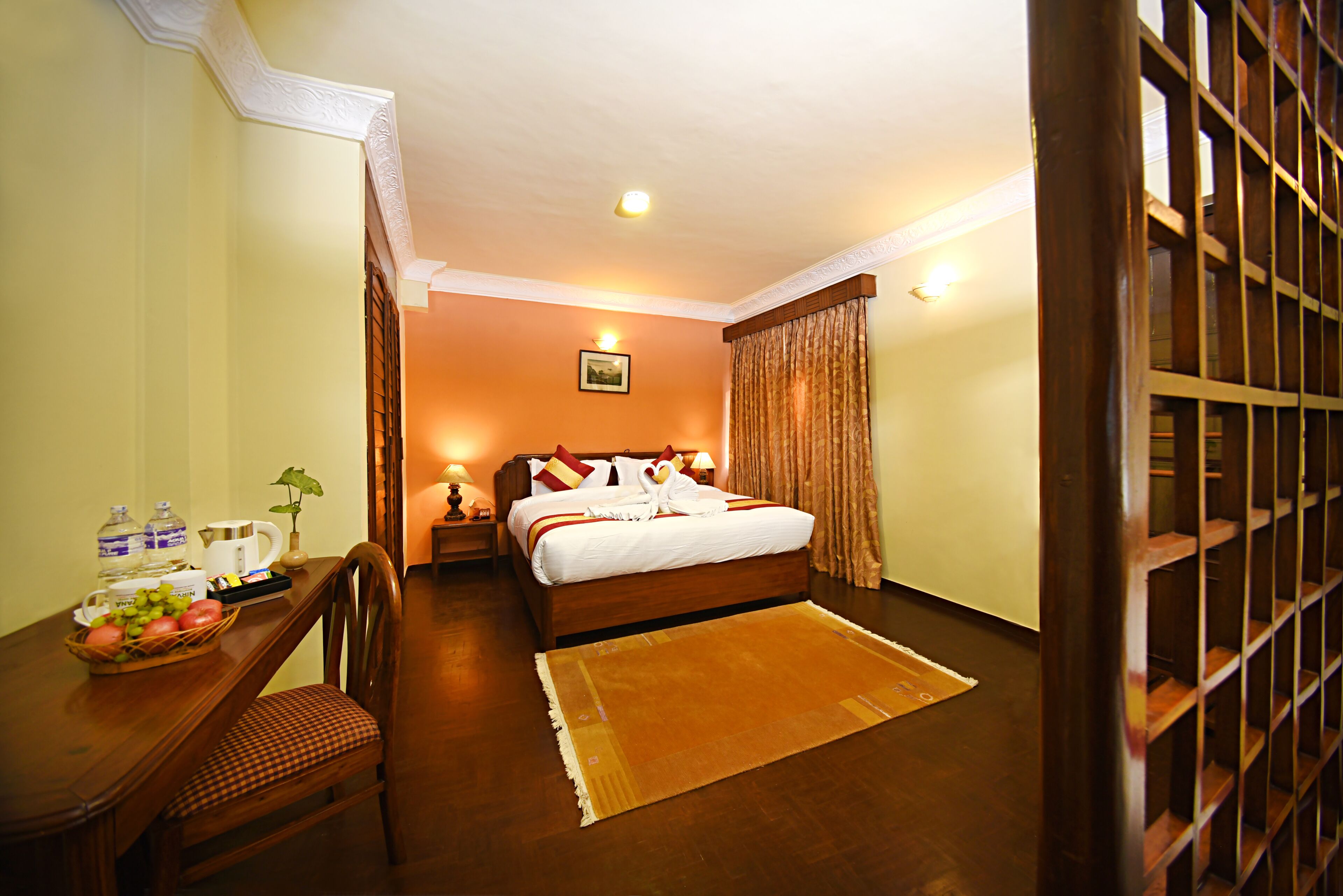 A hotel room with a wooden bed, a dining table with breakfast items, and a view of the outside through a window with curtains.