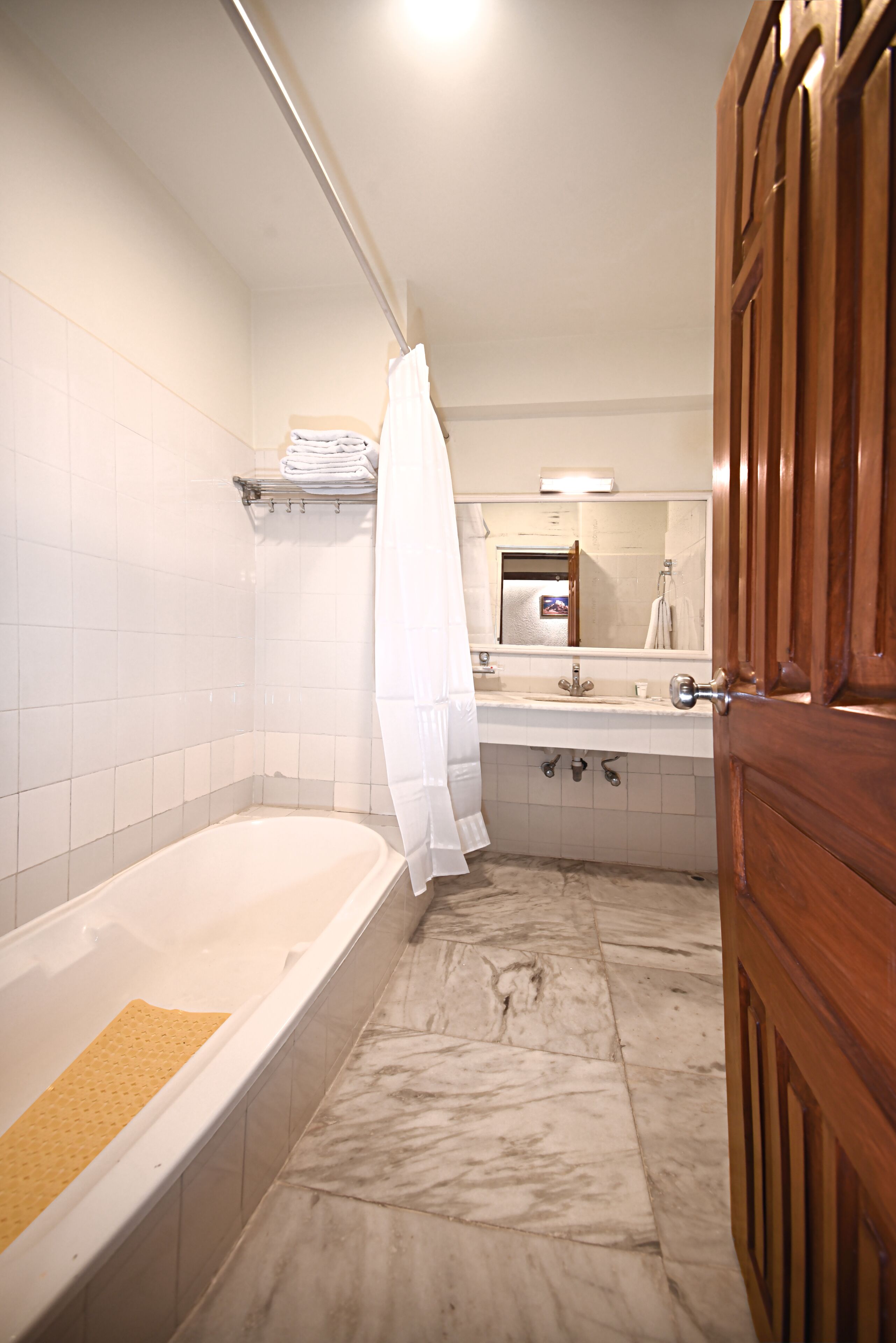 A bathroom with a bathtub, a sink, a mirror, and a wooden door.