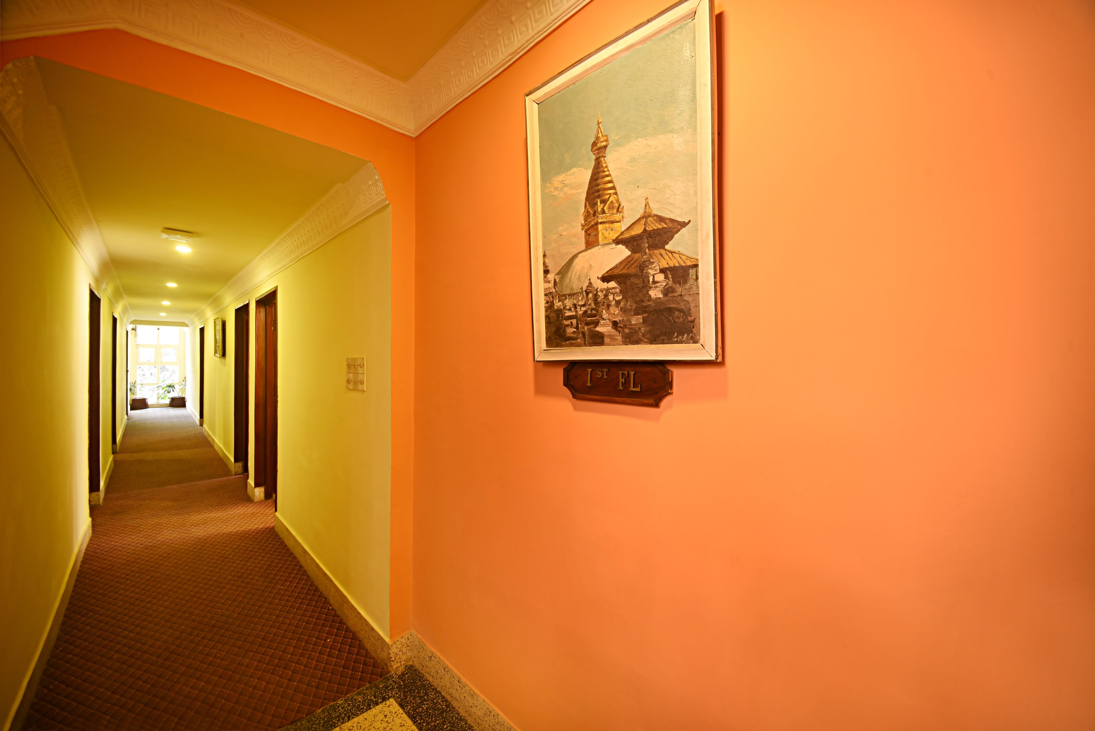 A hotel hallway with a tiled floor, a framed picture of a building, and a sign reading "1st FL".