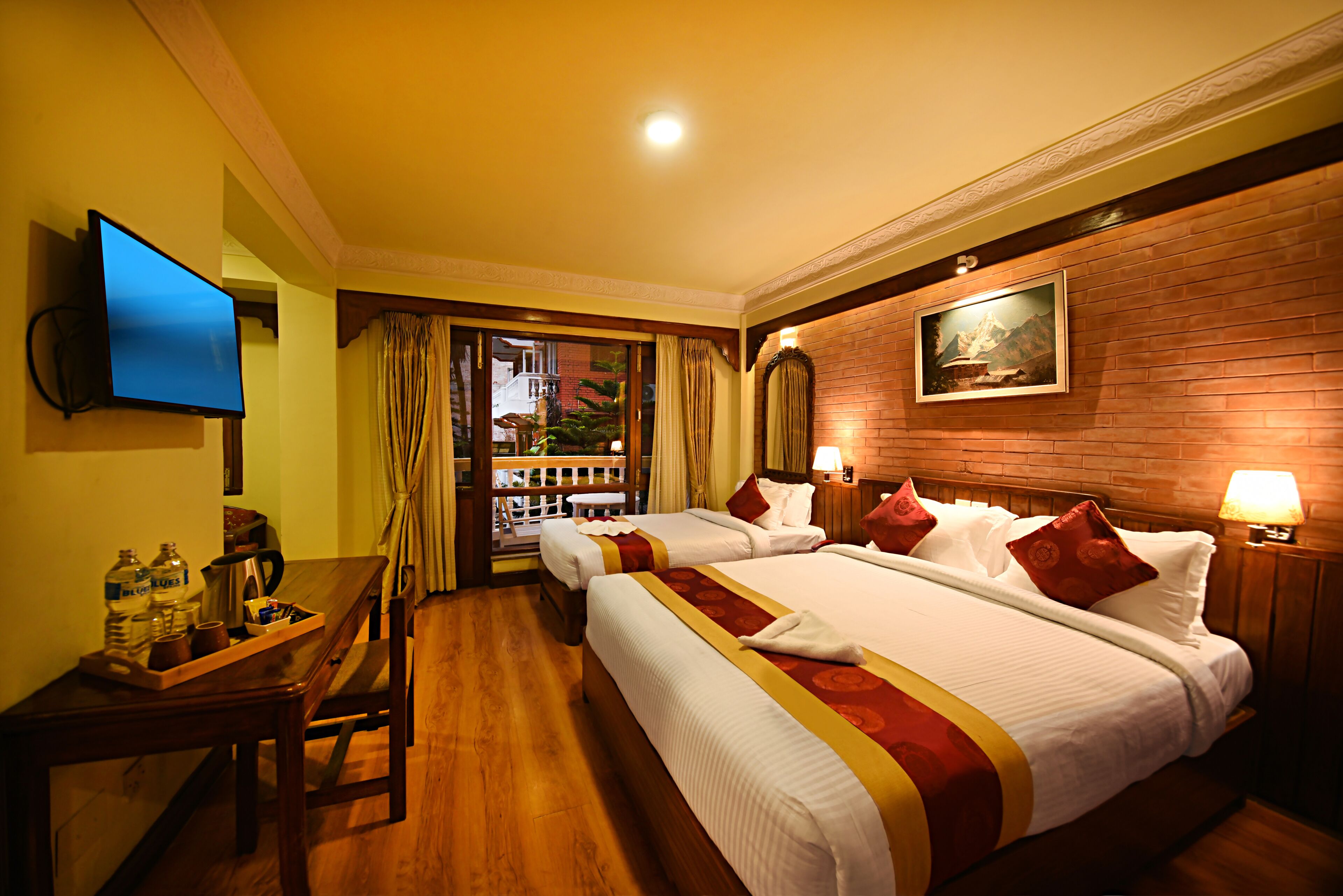 A hotel room with two beds, a TV, a desk with a tray of items, and a view of the outside.