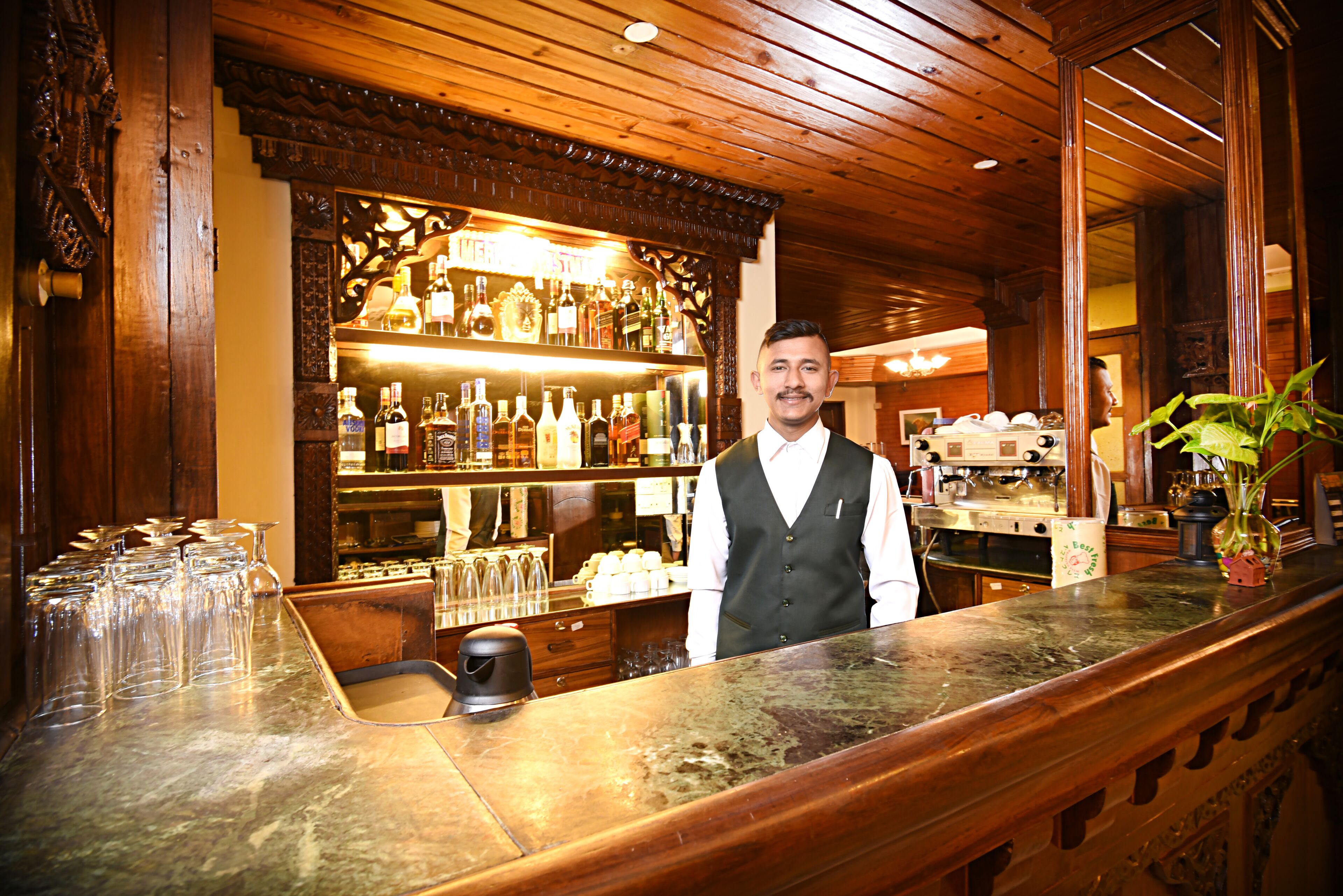Una zona de bar con mostrador de madera, estantes con botellas y una máquina de café.