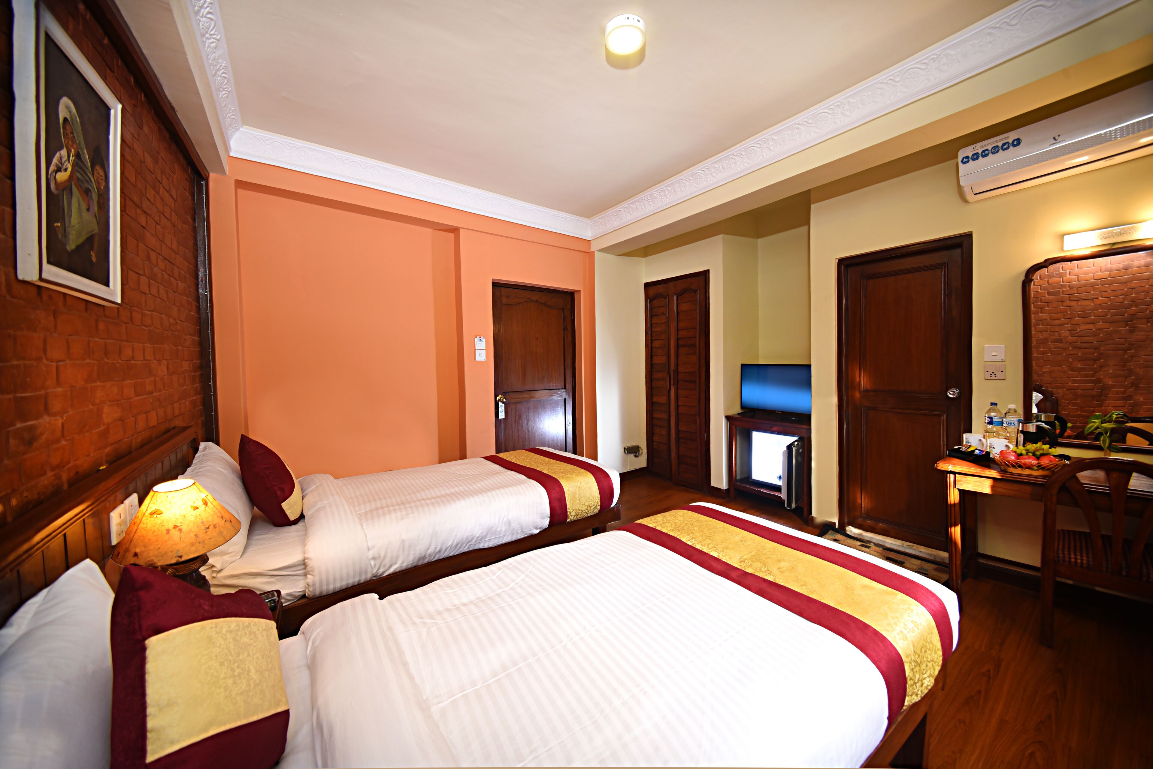 A hotel room with two beds, a television, a desk with a computer, and an air conditioning unit.