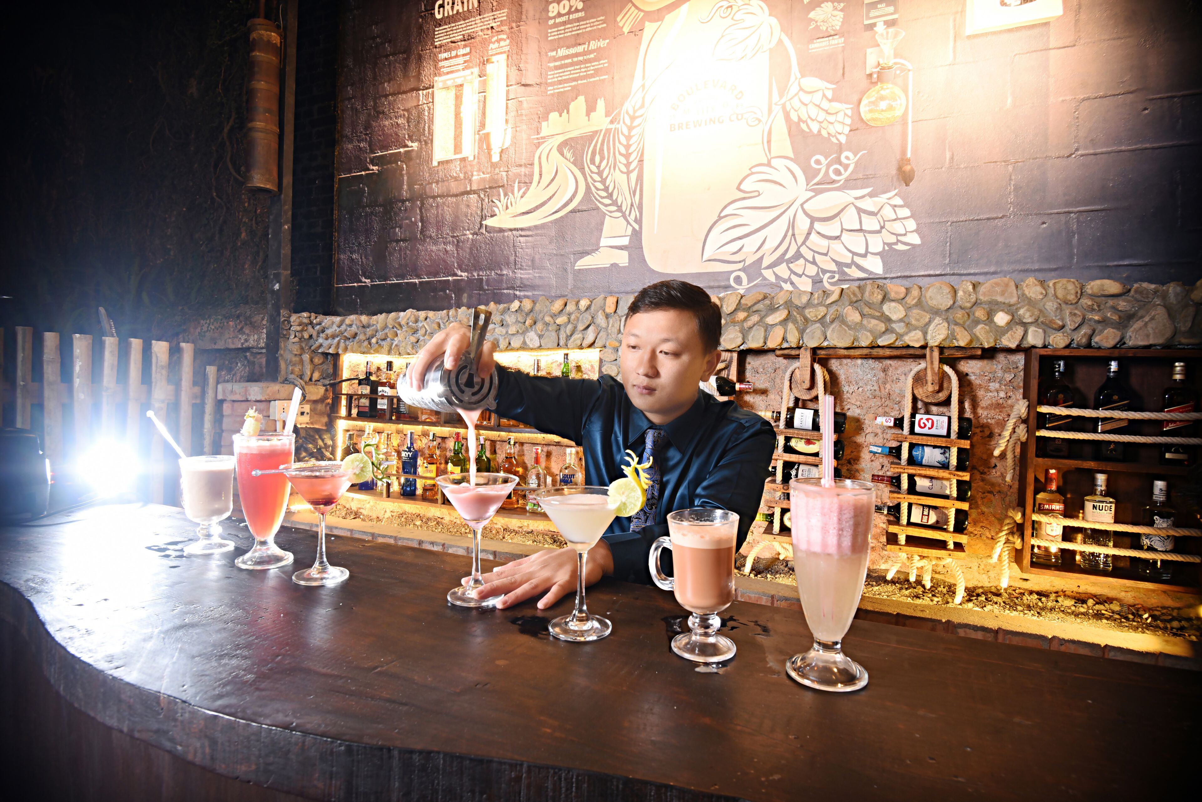 Un cantinero preparando bebidas en un bar con una pared de piedra rústica y una grifo de cerveza grande al fondo.