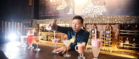 Un cantinero preparando bebidas en un bar con una pared de piedra rústica y una grifo de cerveza grande al fondo.