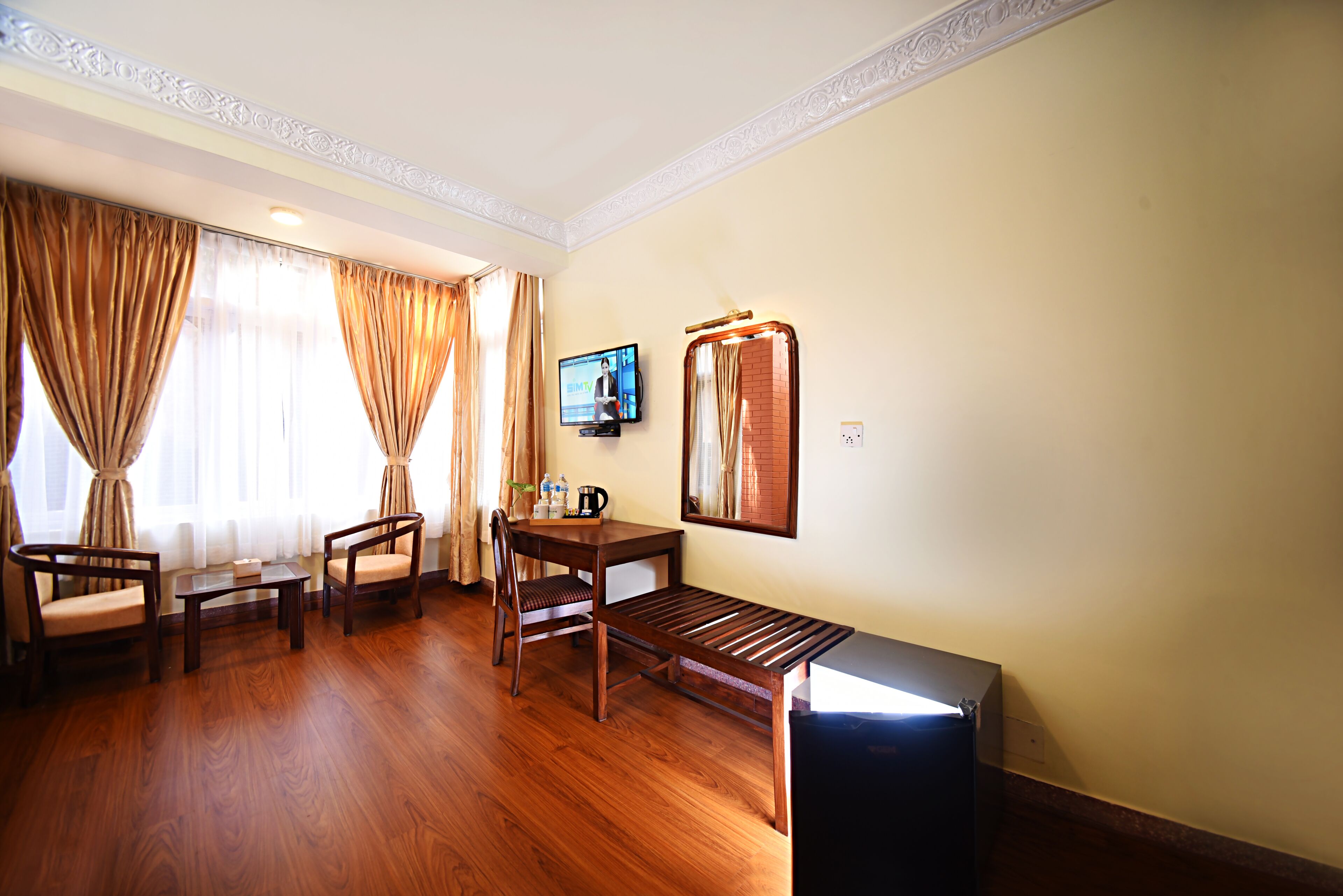 A hotel room with a wooden floor, a desk with a chair, a television, and a bed.