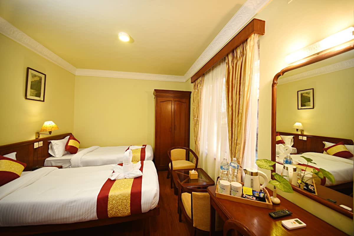 Une chambre d’hôtel avec deux lits, un bureau, une chaise, un miroir et une porte de salle de bain.