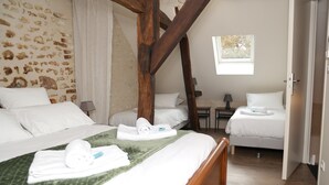 A bedroom with a large bed, two smaller beds, a stone wall, a window, and a wooden ceiling beam. - Gite La Loire 4/5 Personnes à la Campagne Prés des Vergers (Lignières-de-Touraine)