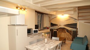 A compact kitchen with a dining area, a sofa, and a staircase leading to an upper level. - Gite La Loire 4/5 Personnes à la Campagne Prés des Vergers (Lignières-de-Touraine)