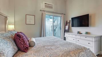 A bedroom with a large bed, a dresser, a flat-screen TV, and a window with curtains.