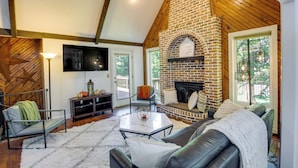 Un salon chaleureux avec une cheminée en briques, un téléviseur à écran plat fixé au mur et un coin salon confortable avec un canapé et des fauteuils.