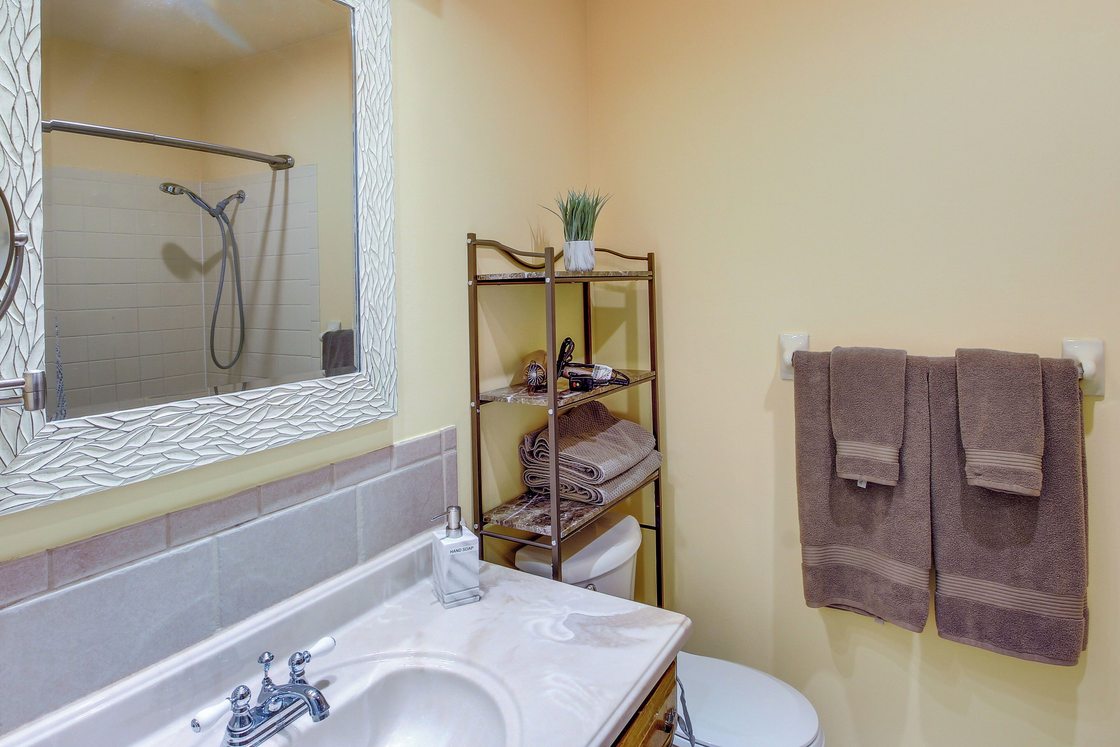 A bathroom with a bathtub, a toilet, a sink, a mirror, and a shelf with towels.