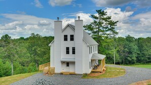 Uma casa grande e branca, com dois andares, uma chaminé notável, um alpendre e uma pequena construção anexa.