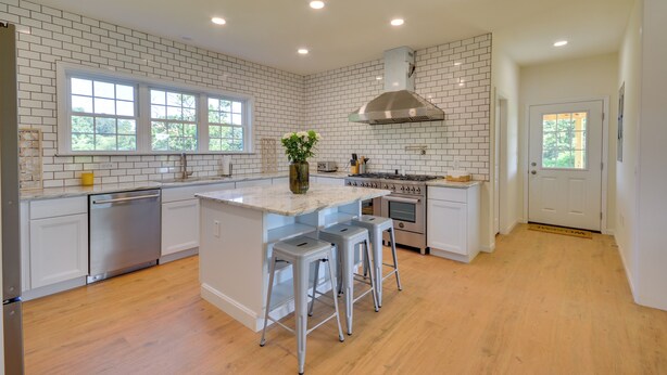 Cozinha moderna com azulejos brancos tipo metrô, eletrodomésticos de aço inoxidável e uma ilha grande com banquetas.