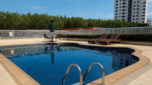 A swimming pool with a tiled deck, lounge chairs, and a fenced area. - Flat Próximo ao Riocentro - Barra da Tijuca (Rio de Janeiro)