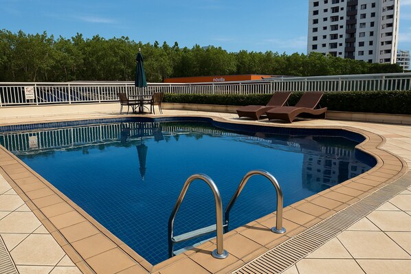A swimming pool with a tiled deck, lounge chairs, and a fenced area. - Flat Próximo ao Riocentro - Barra da Tijuca (Rio de Janeiro)