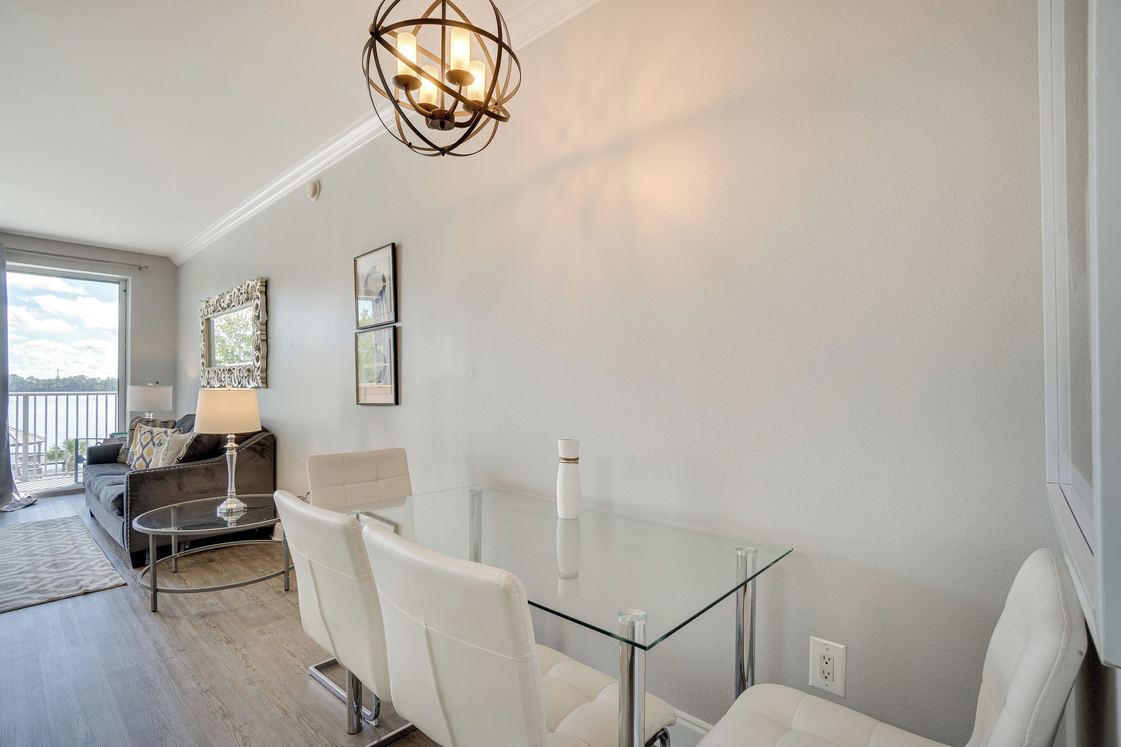 A modern living room with a glass table, white leather chairs, a sofa, and a chandelier.
