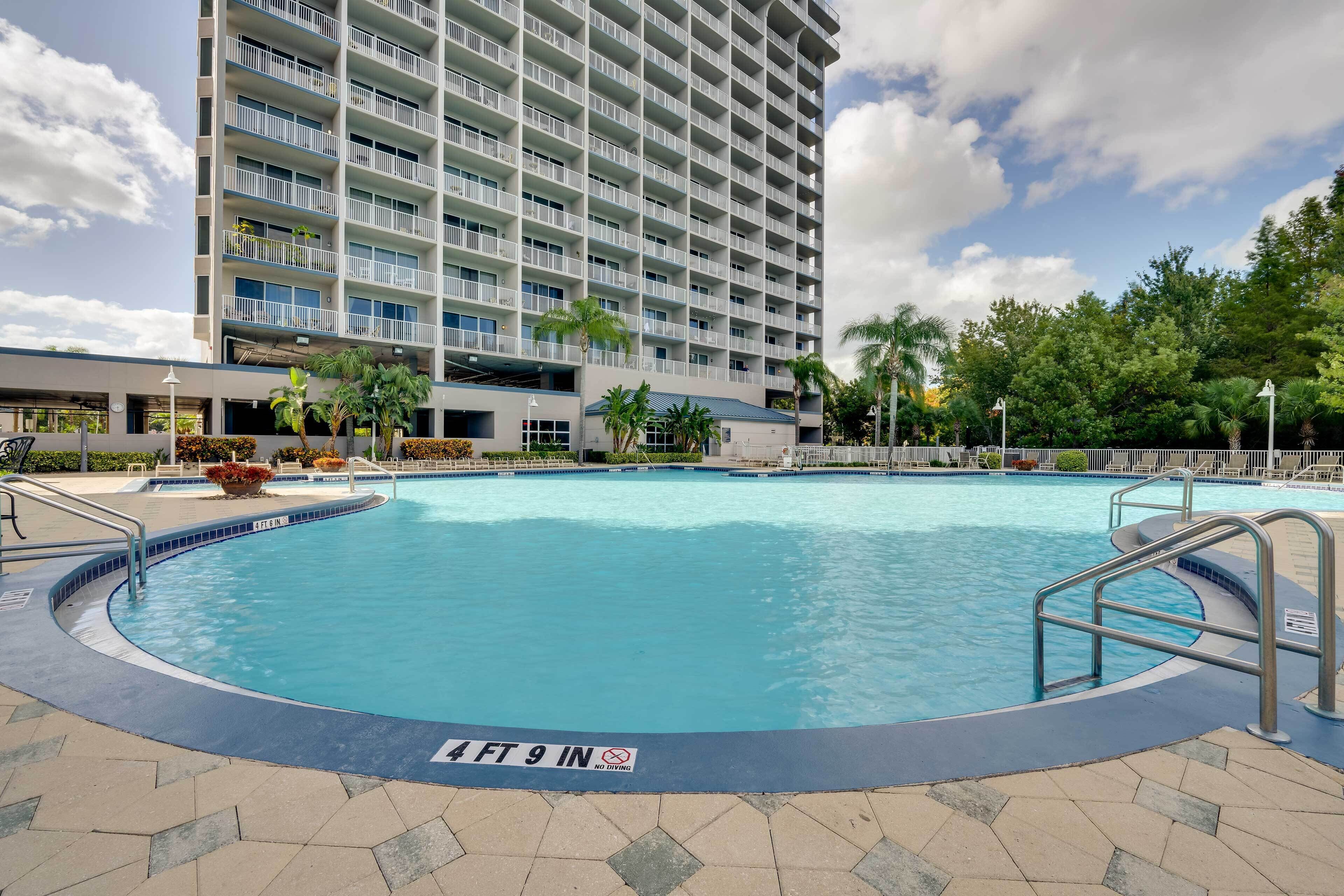 A hotel pool with a sign indicating a depth of 4 ft 9 in, surrounded by a building with multiple balconies and palm trees.