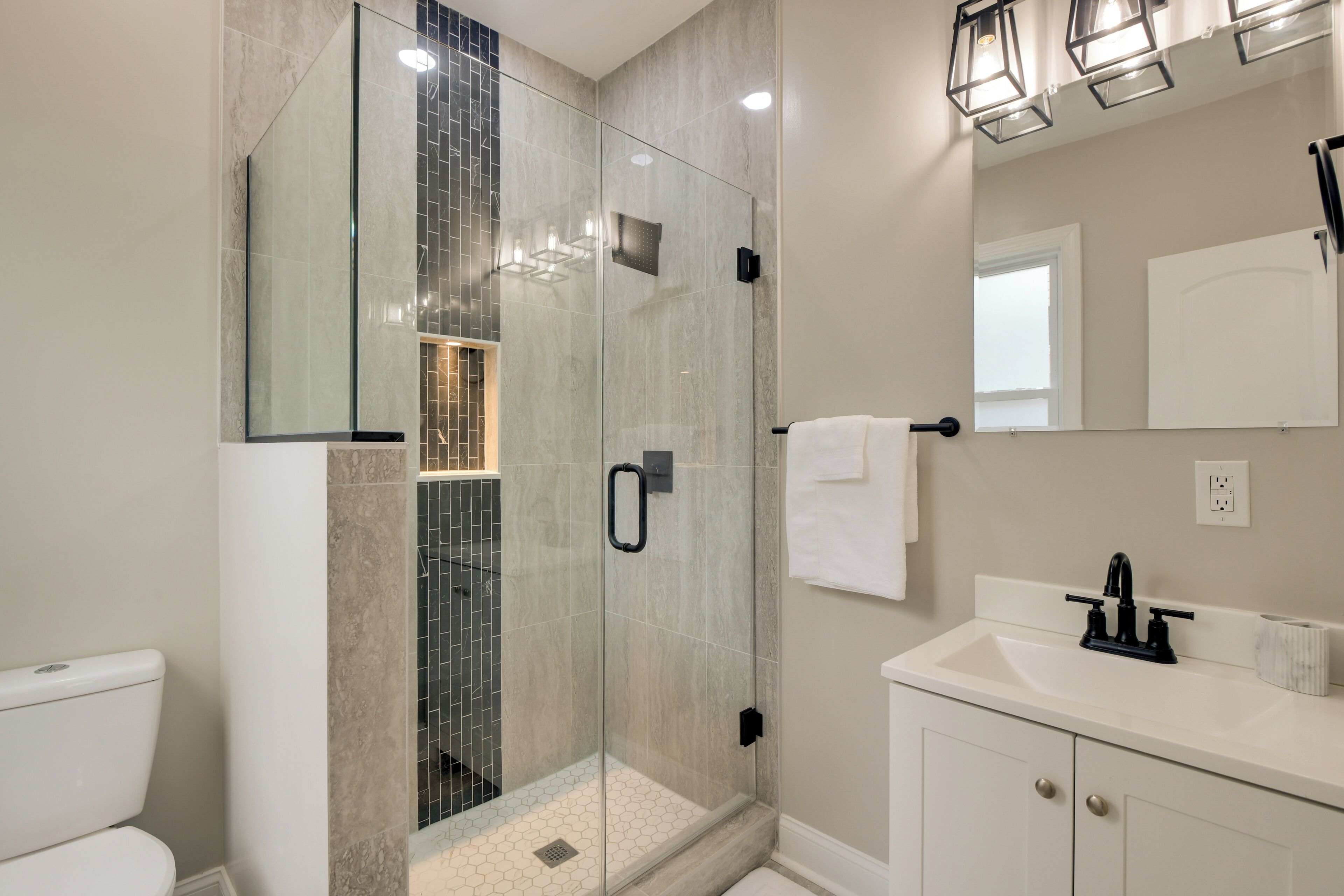 A modern bathroom with a glass-enclosed shower, a white sink, and a large mirror.