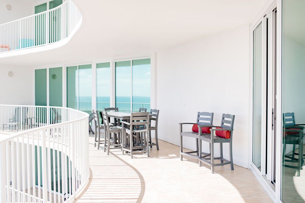 Un balcón moderno con zona de comedor, barandilla blanca y vista al mar.