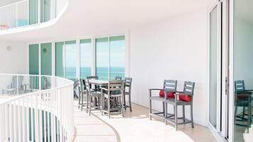 Un balcón moderno con zona de comedor, barandilla blanca y vista al mar.